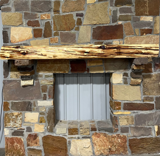Solid live edge cedar fireplace mantel mounted on a stone wall.