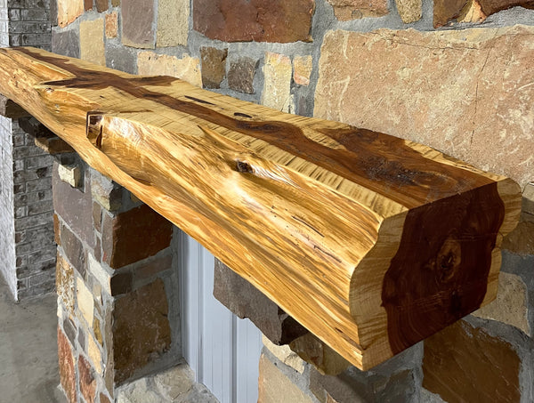 Solid live edge cedar fireplace mantel mounted on a stone wall.