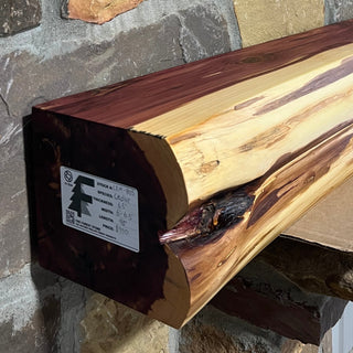 Solid live edge cedar fireplace mantel mounted on a stone wall.
