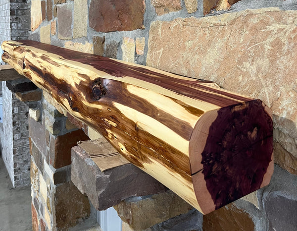 Solid live edge cedar fireplace mantel mounted on a stone wall.
