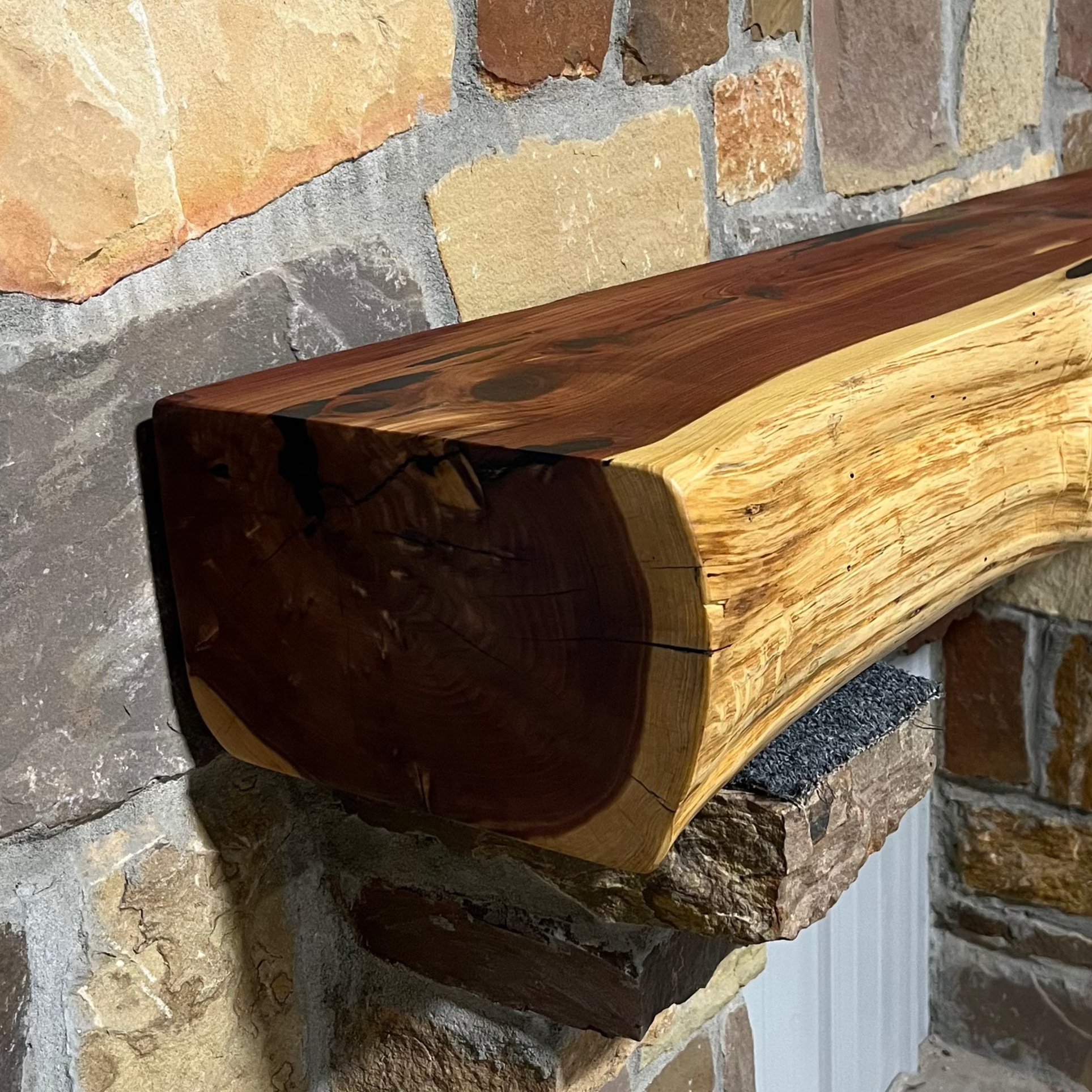 Solid live edge cedar fireplace mantel mounted on a stone wall.
