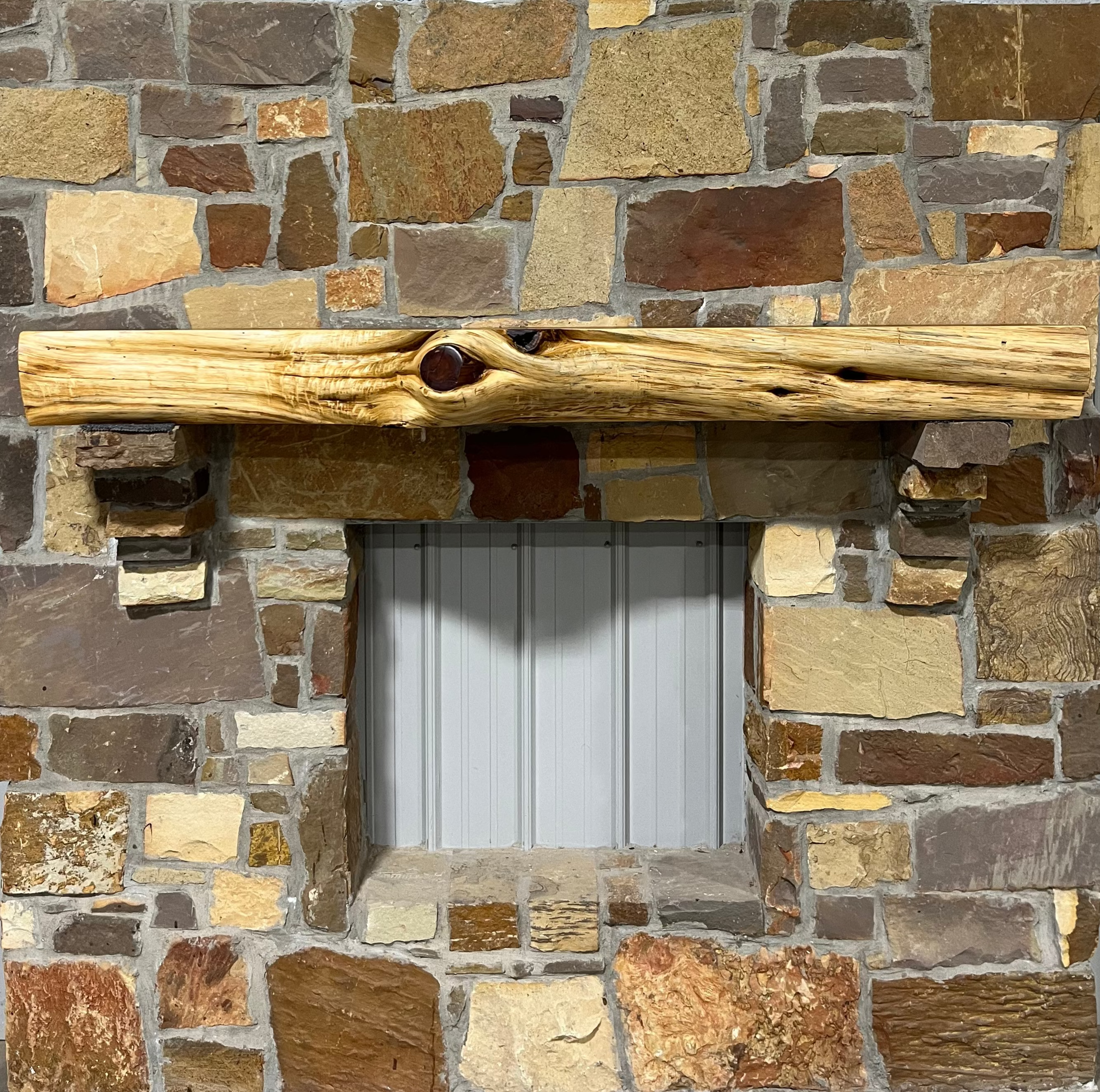 Solid live edge cedar fireplace mantel mounted on a stone wall.

