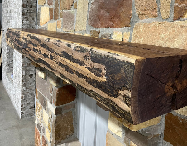 Solid live edge walnut fireplace mantel mounted on a stone wall.