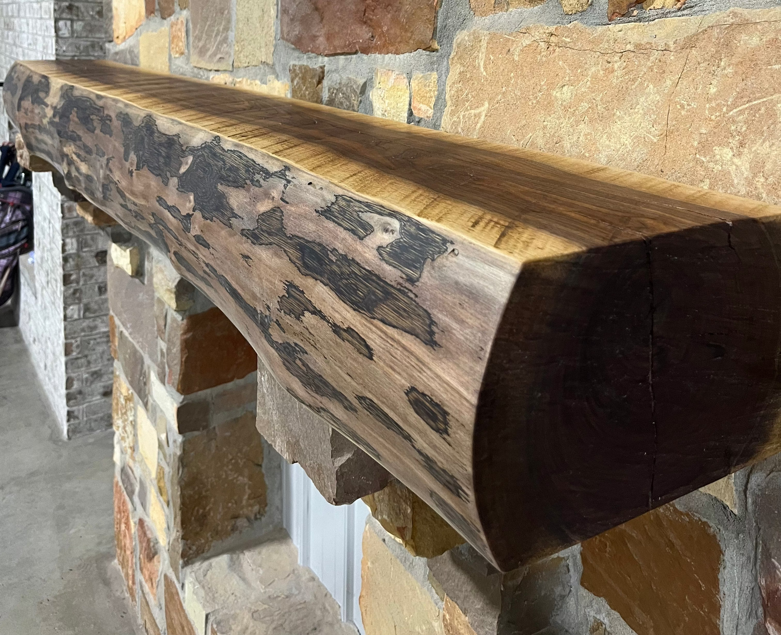 Solid live edge walnut fireplace mantel mounted on a stone wall.