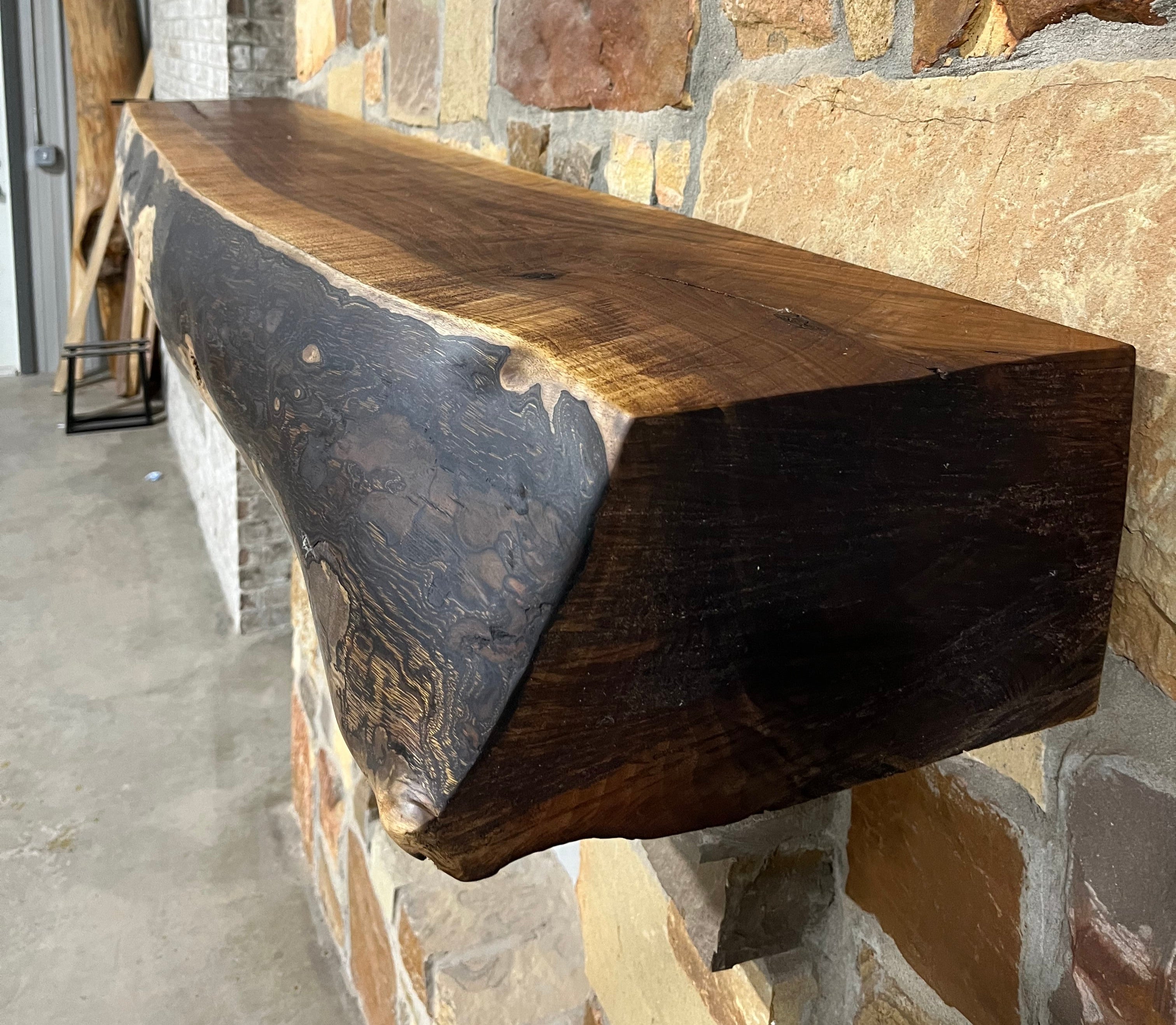 Solid live edge walnut fireplace mantel mounted on a stone wall.
