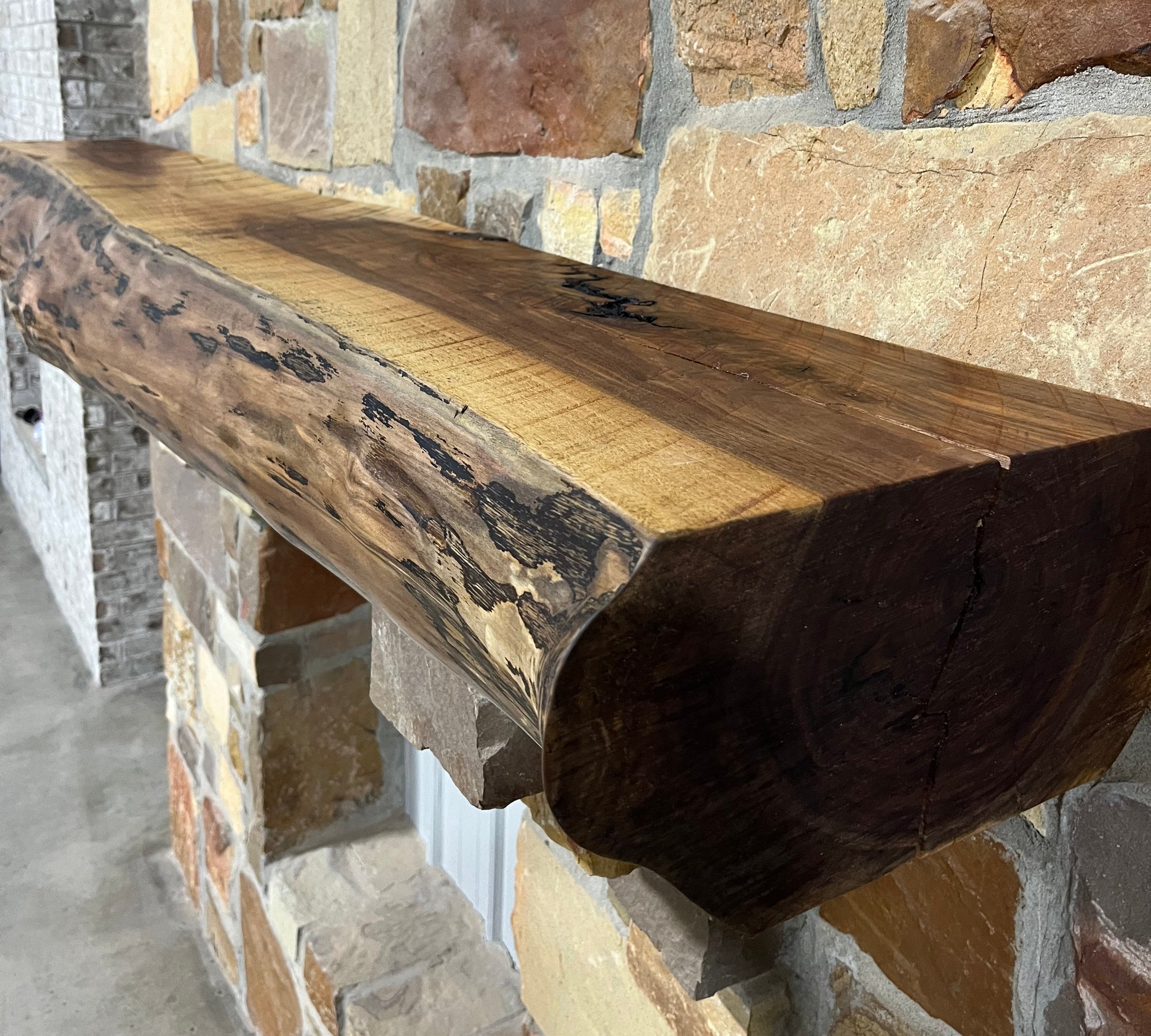 Solid live edge walnut fireplace mantel mounted on a stone wall.