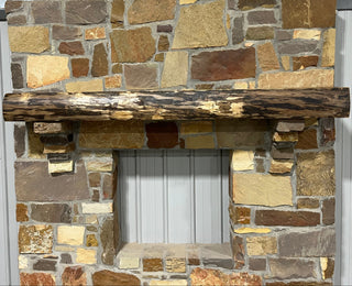 Solid live edge walnut fireplace mantel mounted on a stone wall.