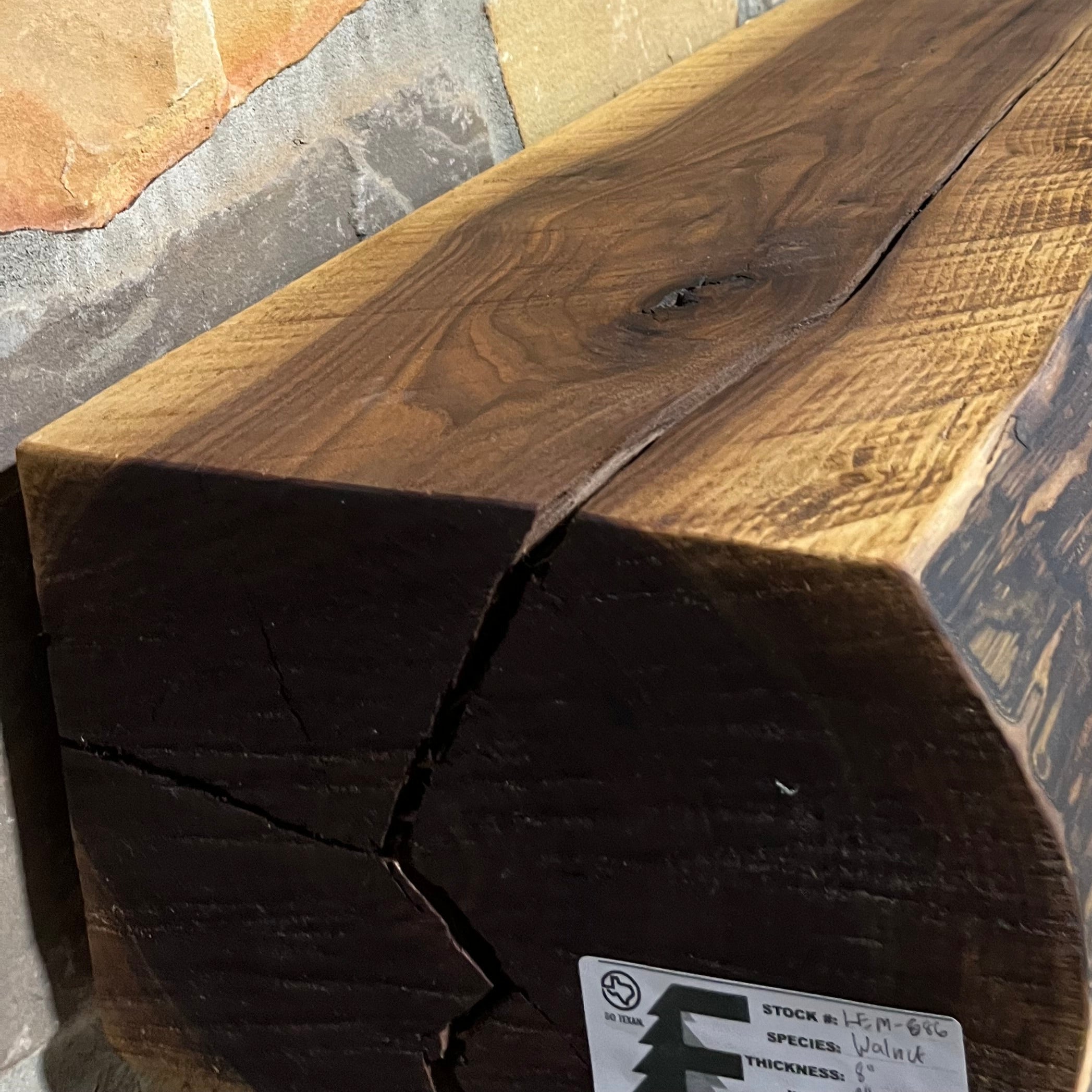Solid live edge walnut fireplace mantel mounted on a stone wall.