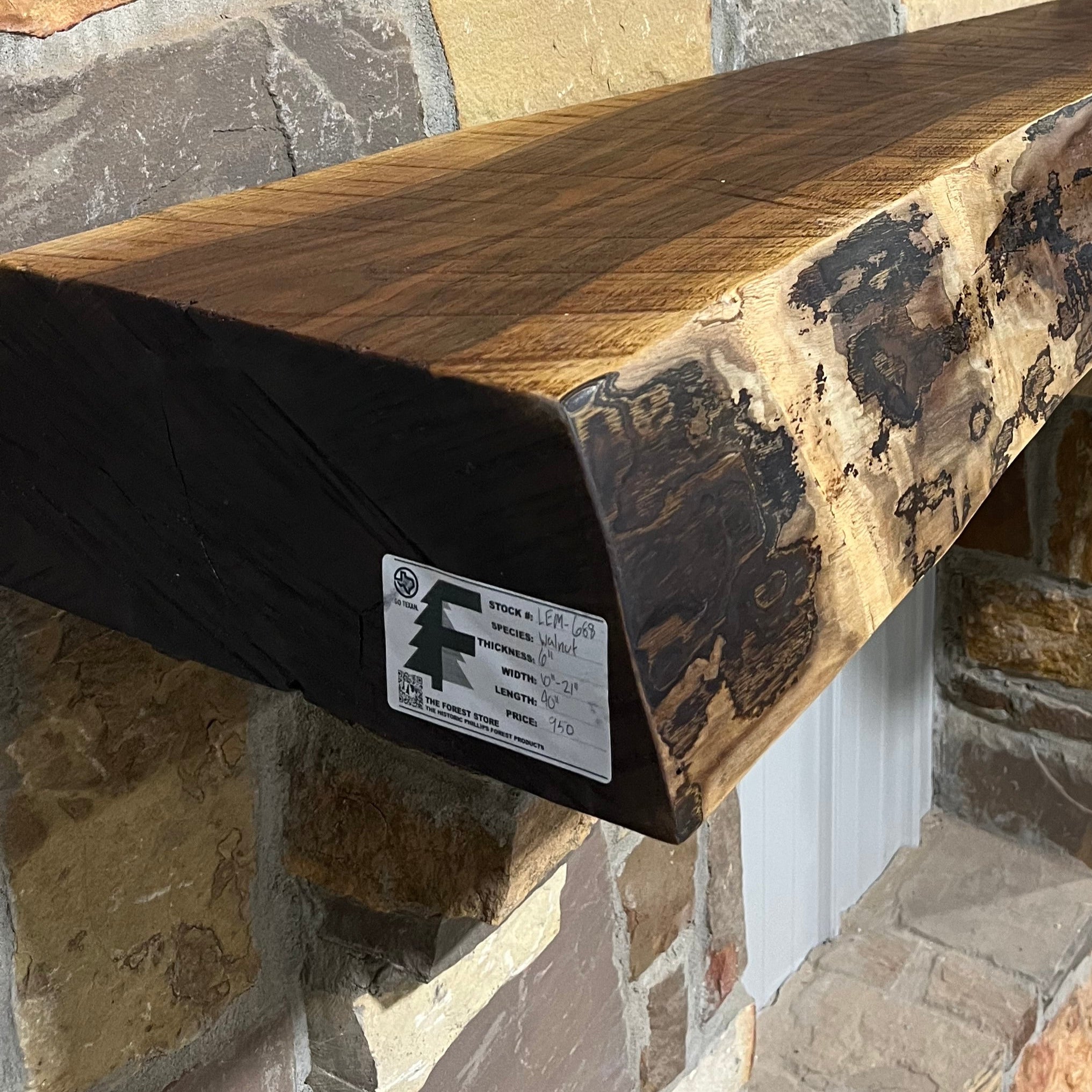 A solid walnut wood fireplace mantel with the side of the tree exposed on a stone wall.