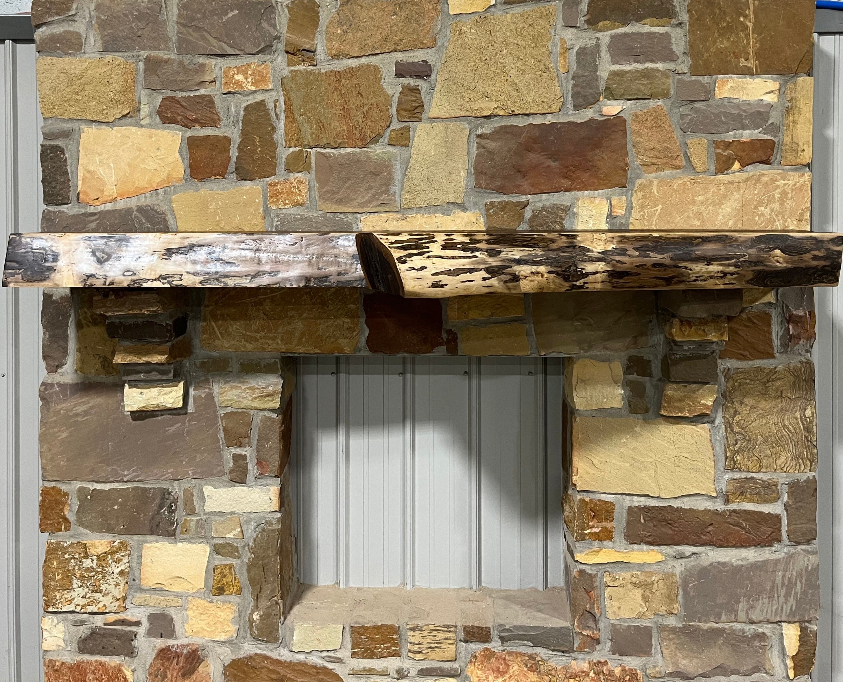 A solid walnut wood fireplace mantel with the side of the tree exposed on a stone wall.