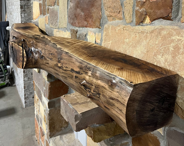 Solid live edge walnut fireplace mantel mounted on a stone wall.