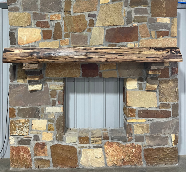 Solid live edge walnut fireplace mantel mounted on a stone wall.