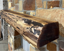 Solid live edge walnut fireplace mantel mounted on a stone wall.