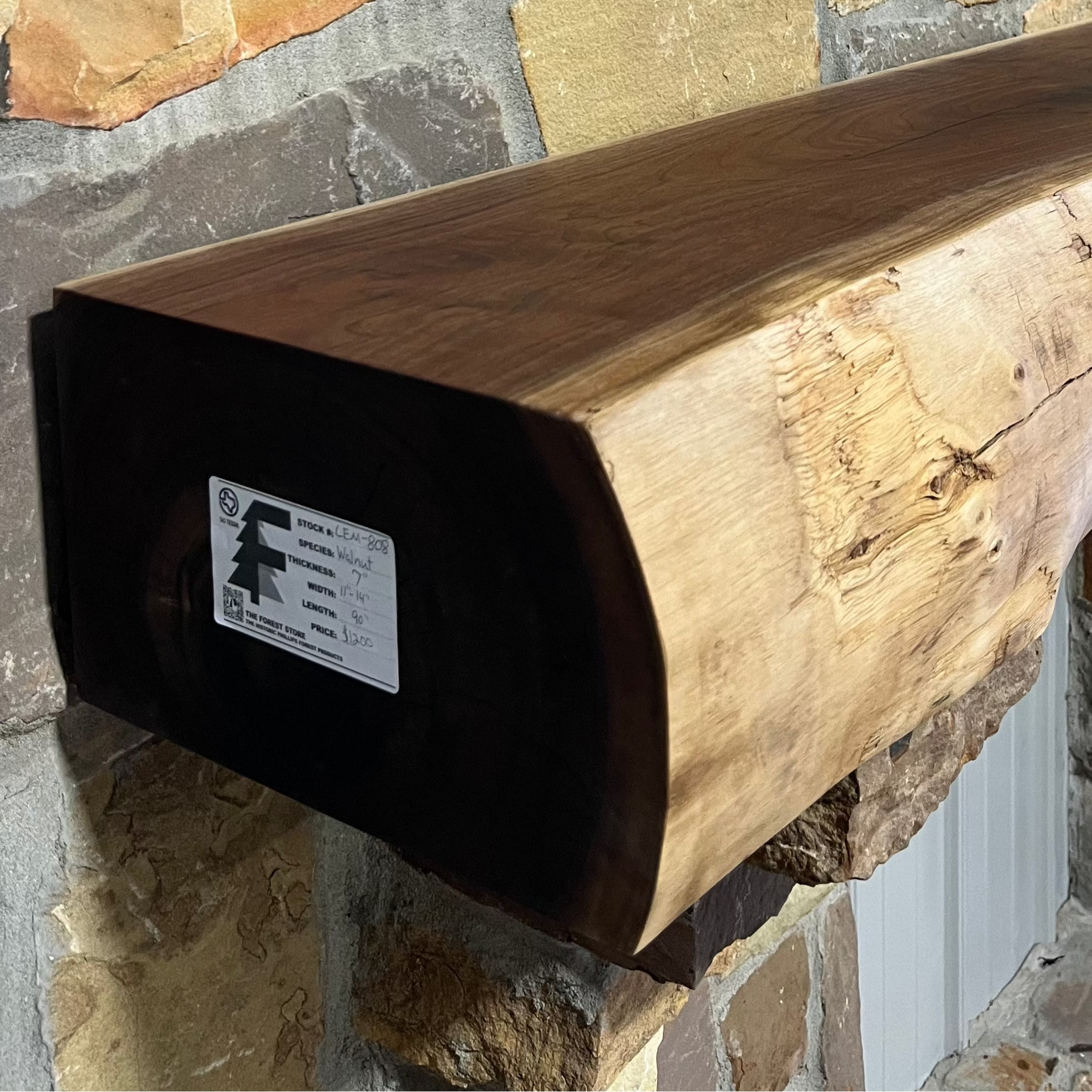 Solid live edge walnut fireplace mantel mounted on a stone wall.