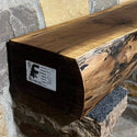 A solid walnut wood fireplace mantel with the side of the tree exposed on a stone wall.