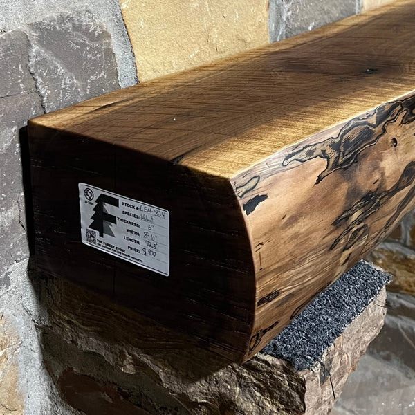A solid walnut wood fireplace mantel with the side of the tree exposed on a stone wall.
