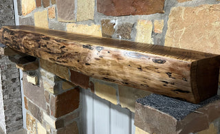 A solid walnut wood fireplace mantel with the side of the tree exposed on a stone wall.