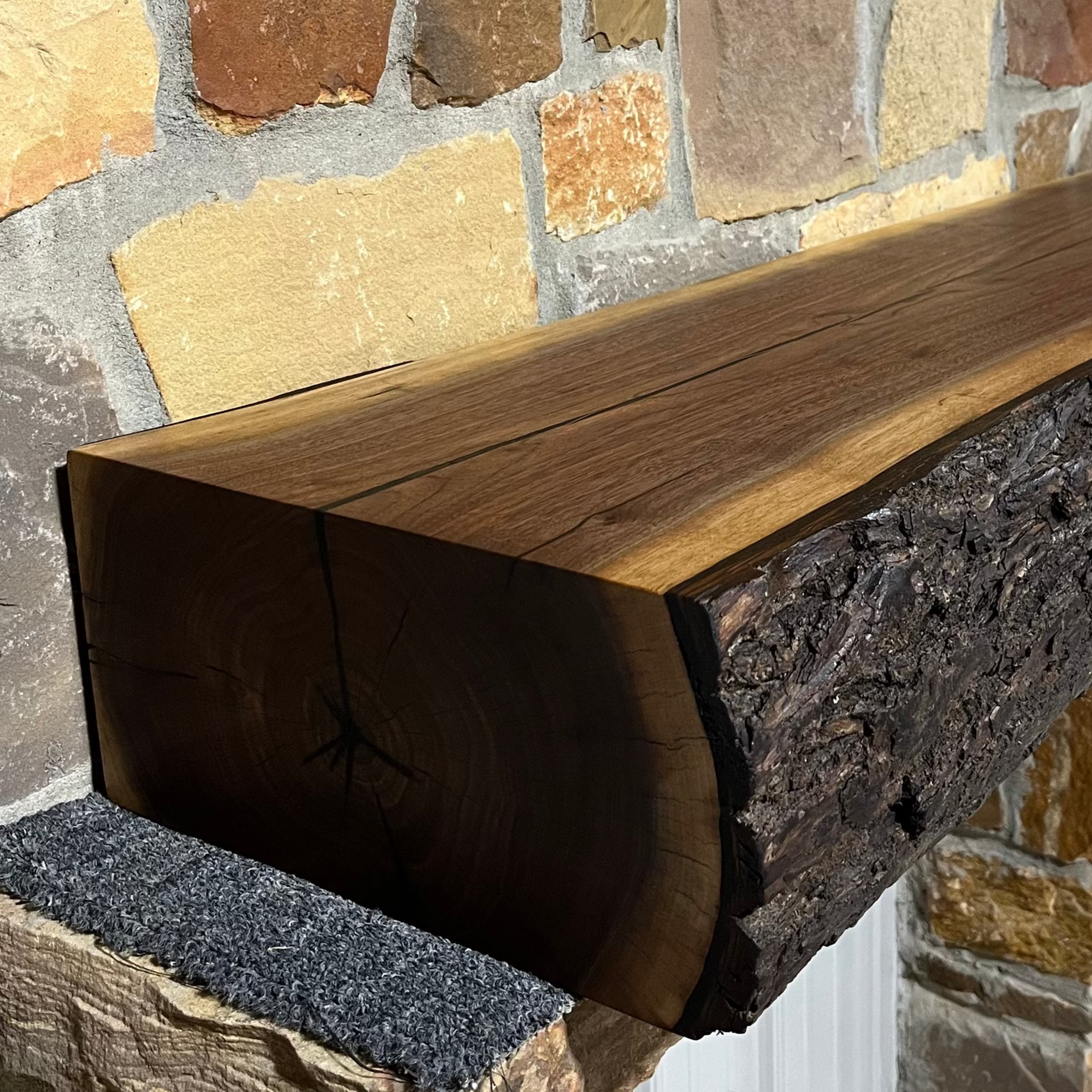 A solid walnut wood fireplace mantel with the side of the tree exposed on a stone wall.