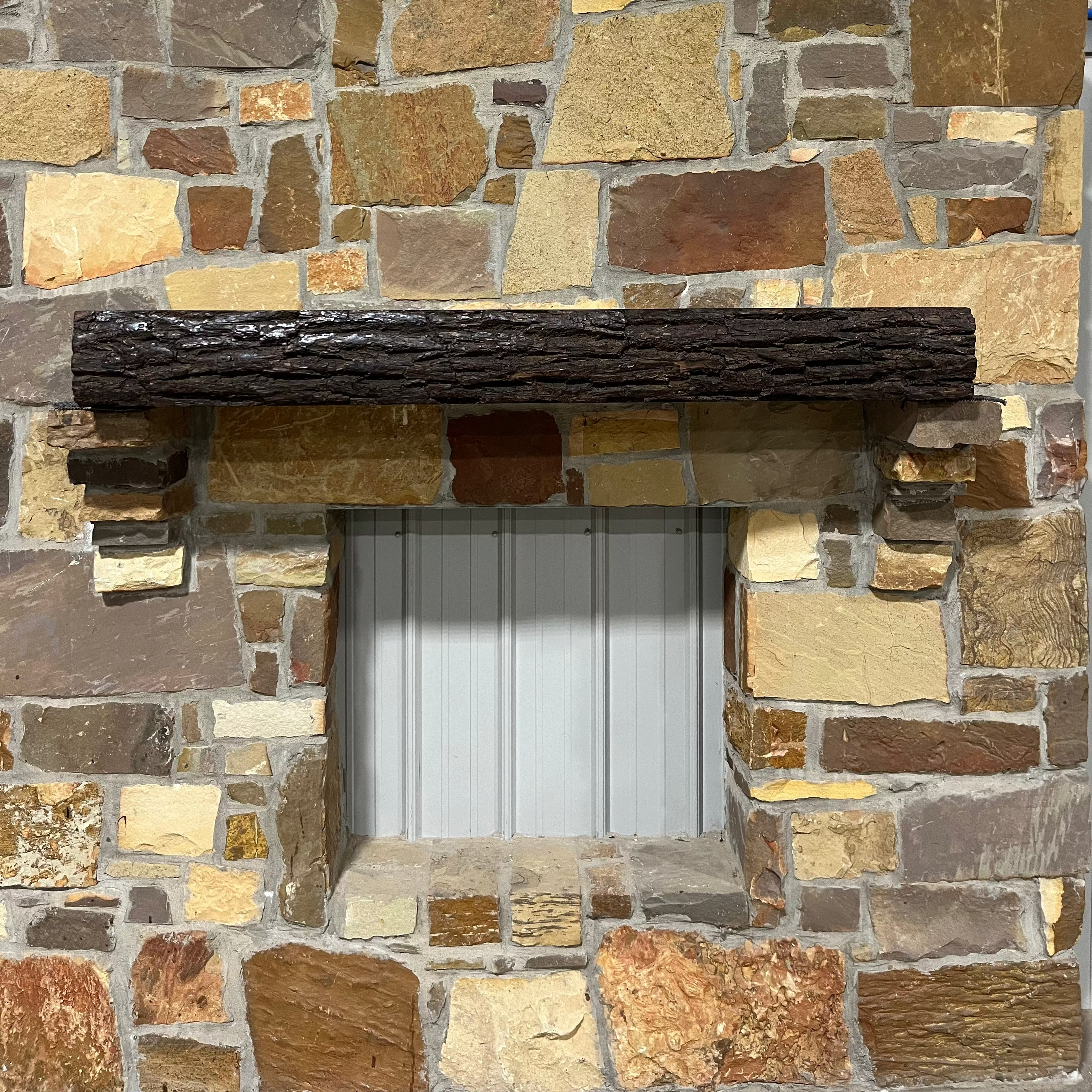 A solid walnut wood fireplace mantel with the side of the tree exposed on a stone wall.