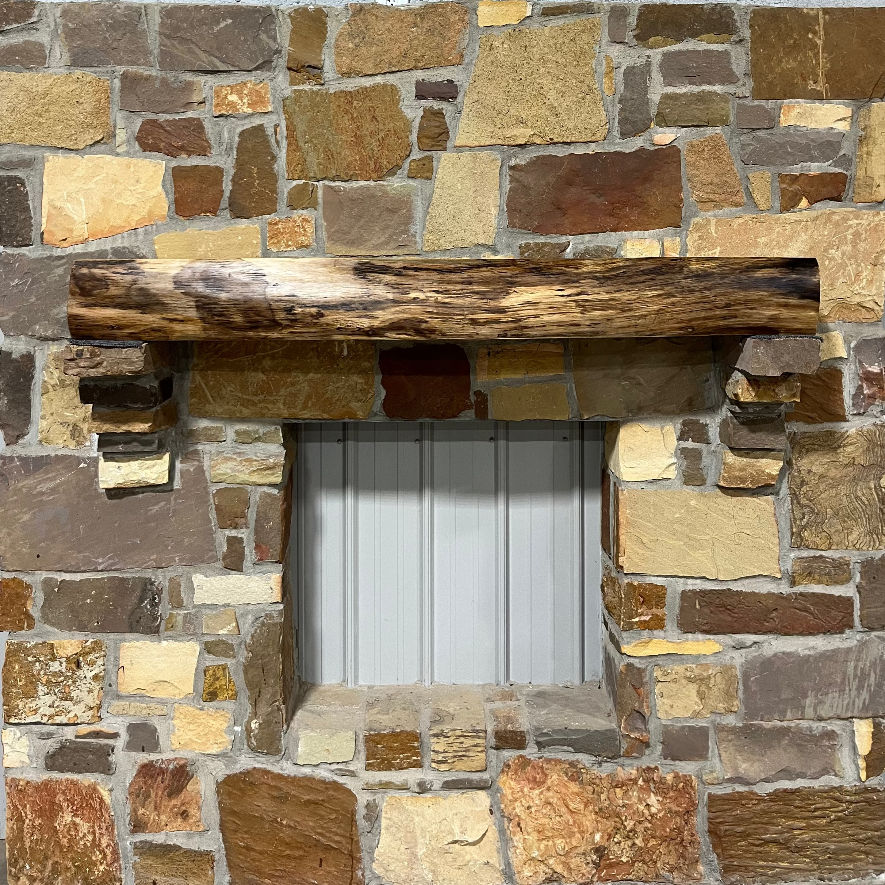 A solid walnut wood fireplace mantel with the side of the tree exposed on a stone wall.