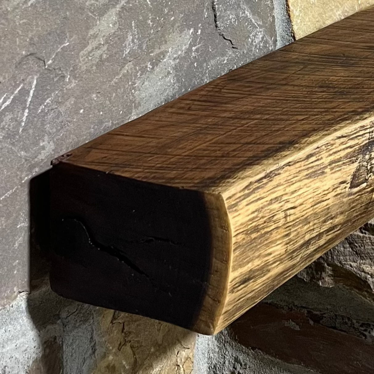 A solid walnut wood fireplace mantel with the side of the tree exposed on a stone wall.
