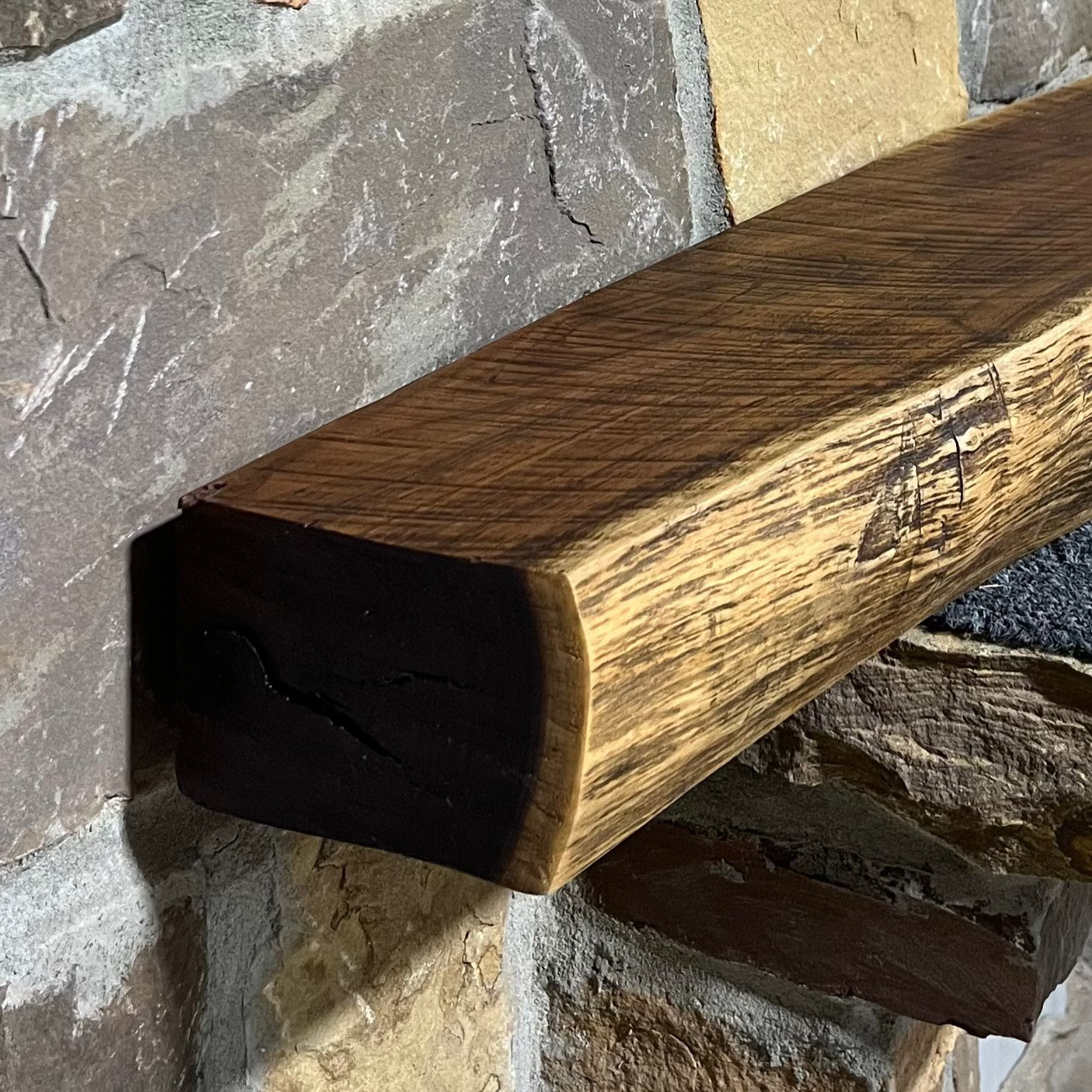 A solid walnut wood fireplace mantel with the side of the tree exposed on a stone wall.