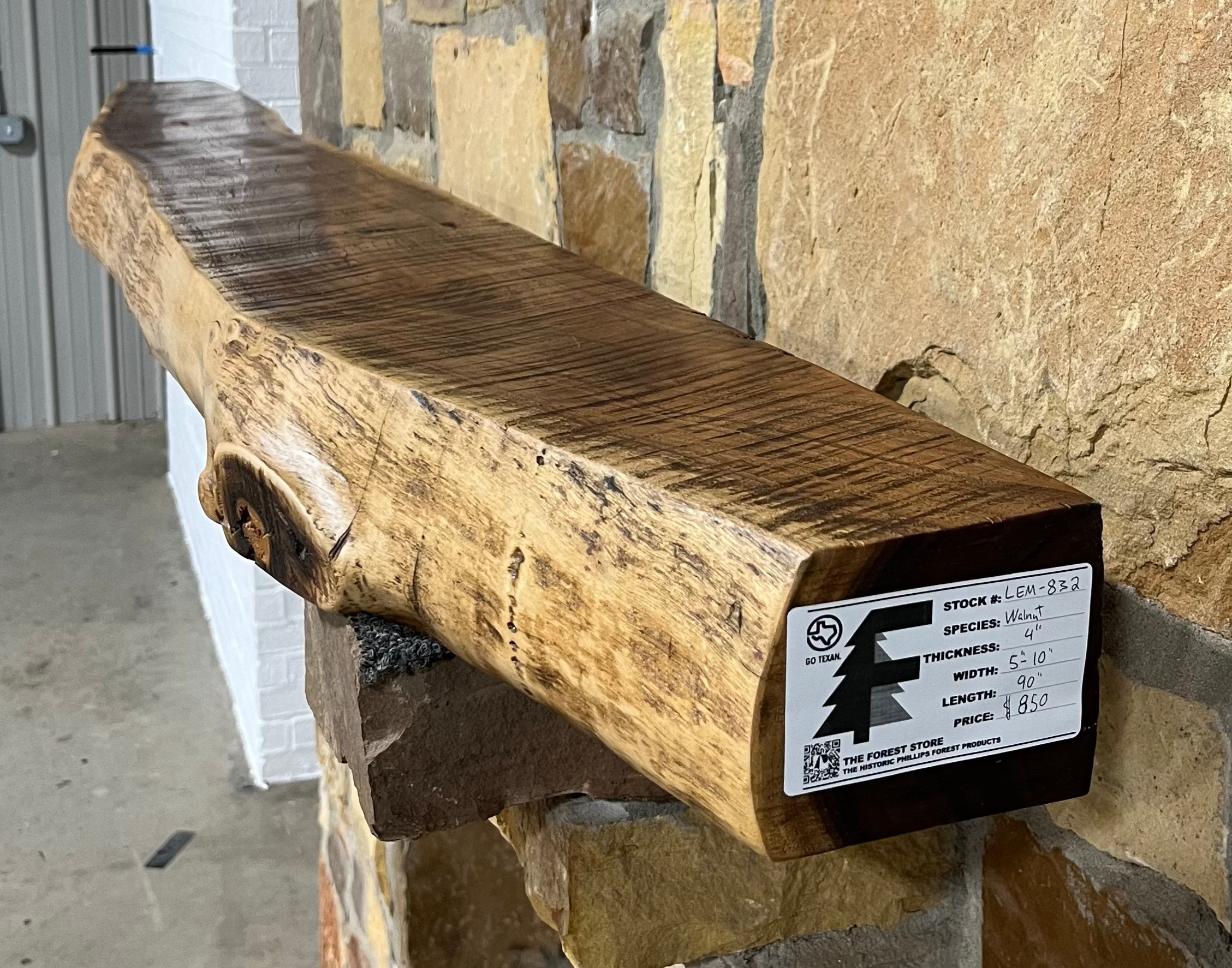 A solid walnut wood fireplace mantel with the side of the tree exposed on a stone wall.