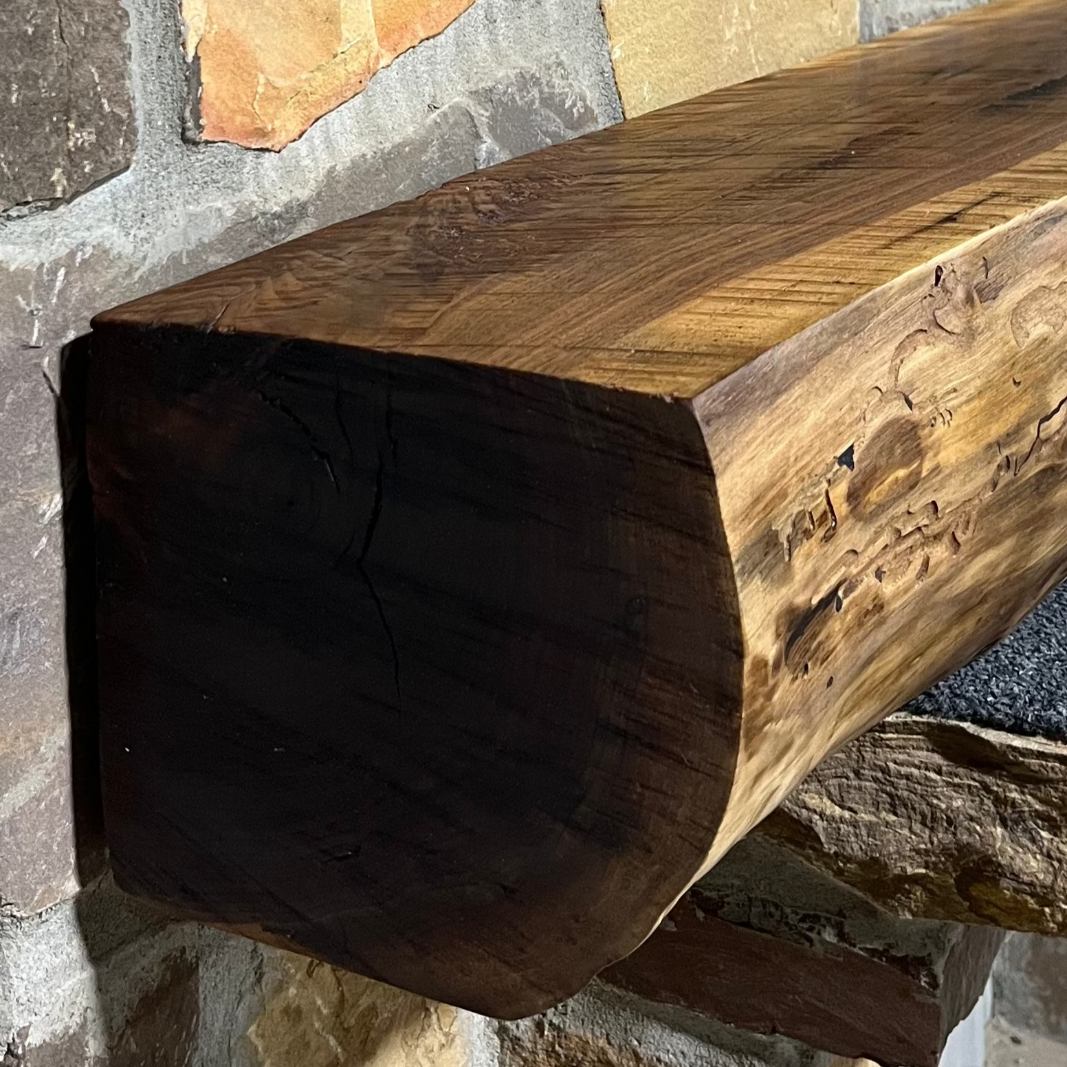 A solid walnut wood fireplace mantel with the side of the tree exposed on a stone wall.