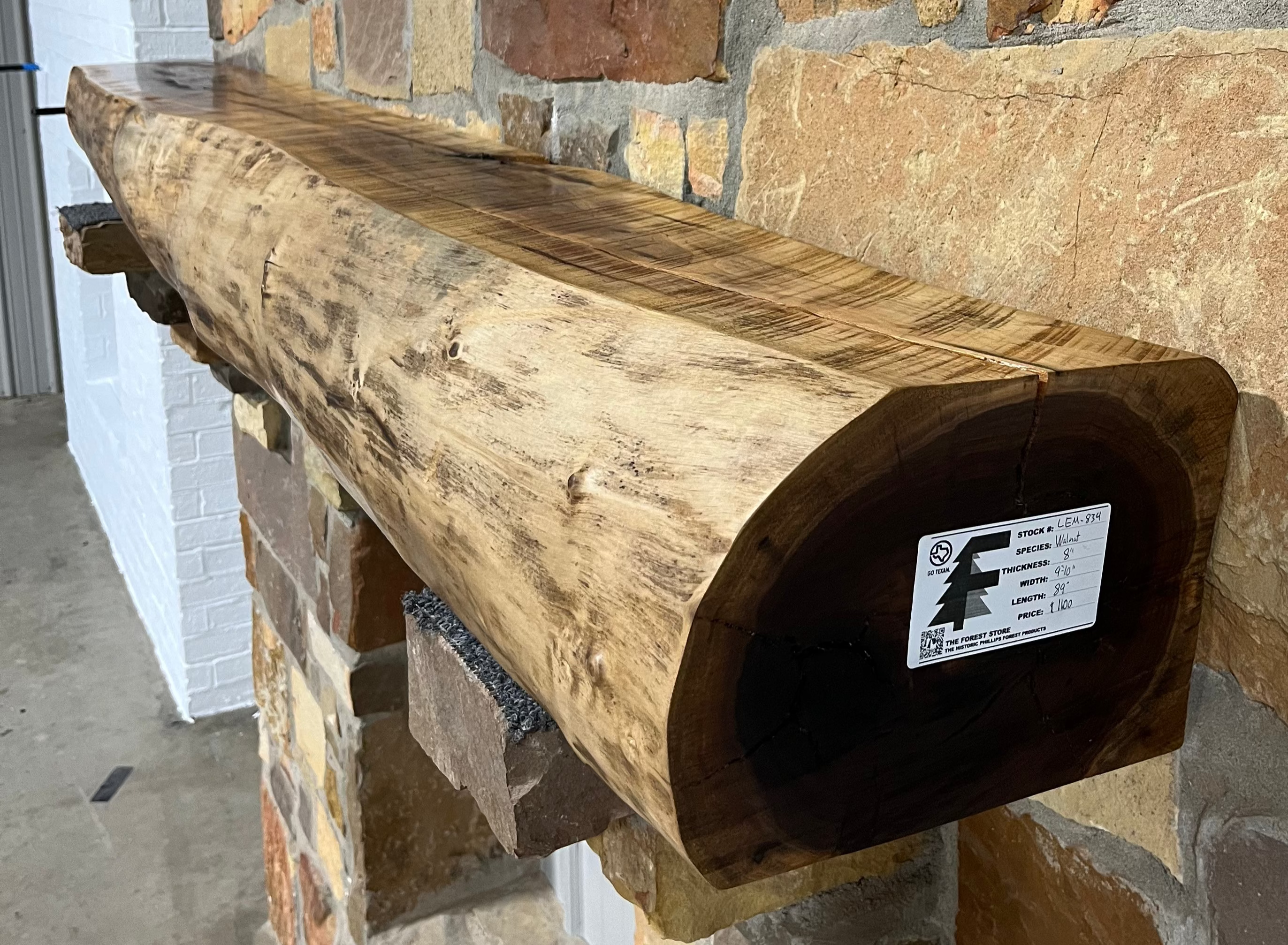 A solid walnut wood fireplace mantel with the side of the tree exposed on a stone wall.
