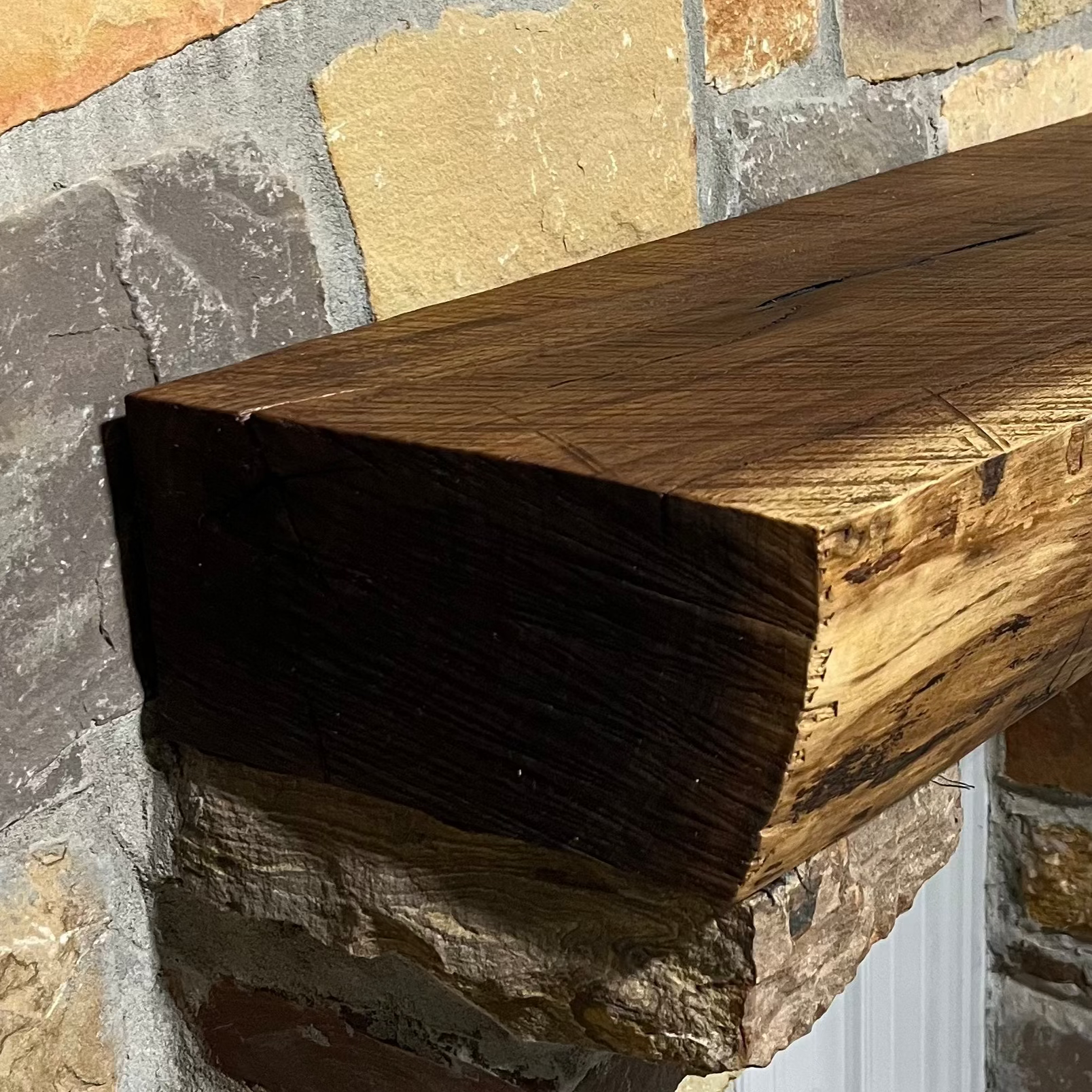 A solid walnut wood fireplace mantel with the side of the tree exposed on a stone wall.