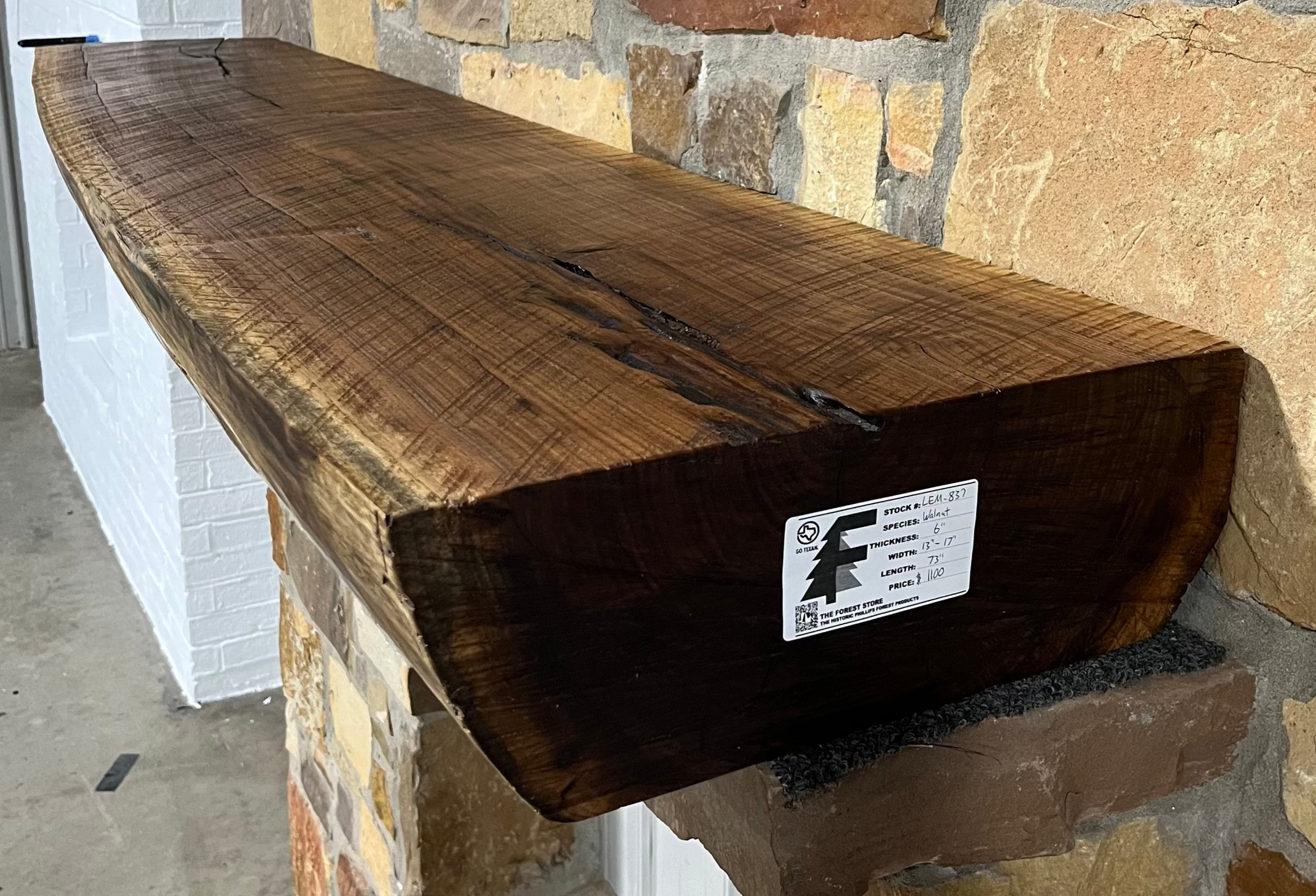 A solid walnut wood fireplace mantel with the side of the tree exposed on a stone wall.