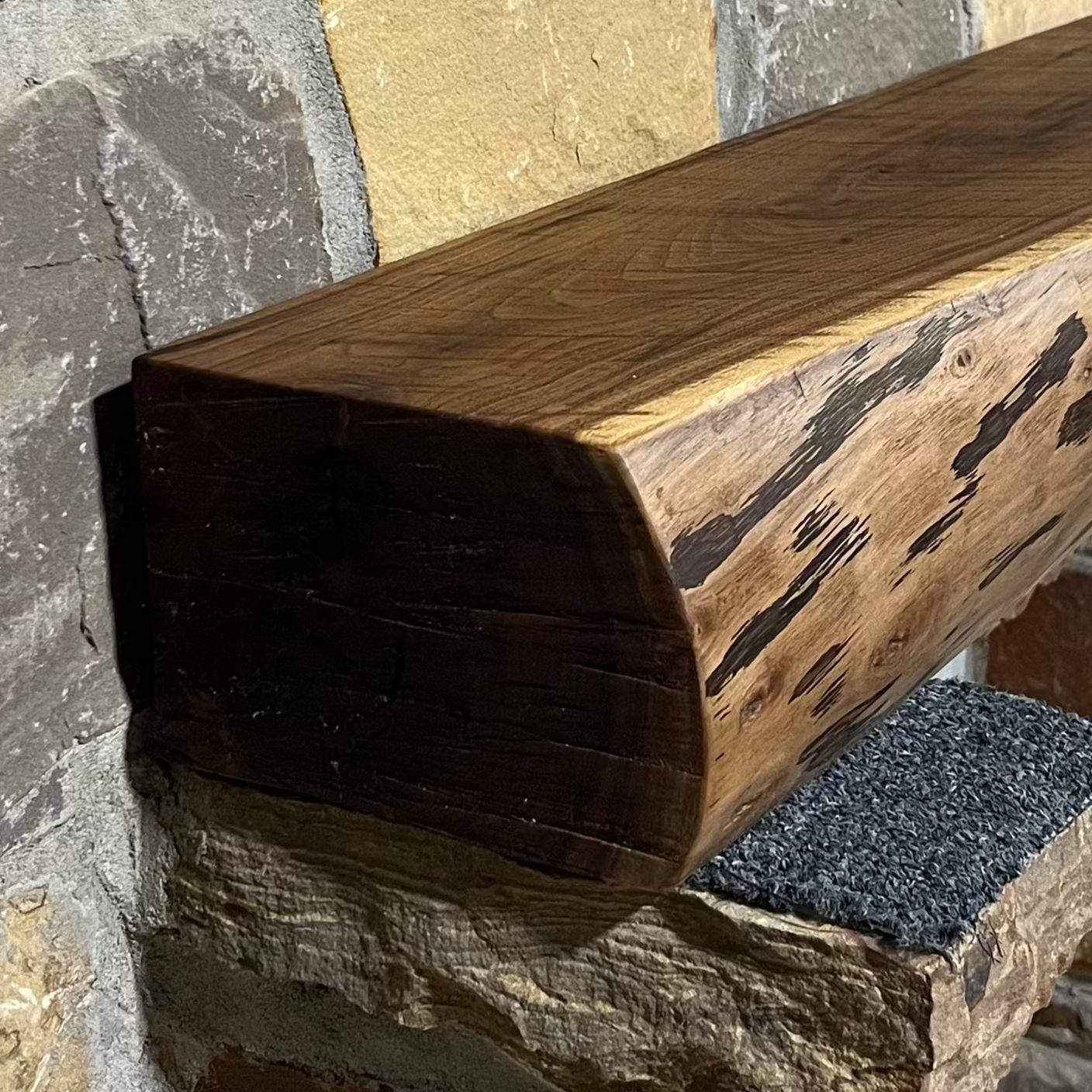 A solid walnut wood fireplace mantel with the side of the tree exposed on a stone wall.