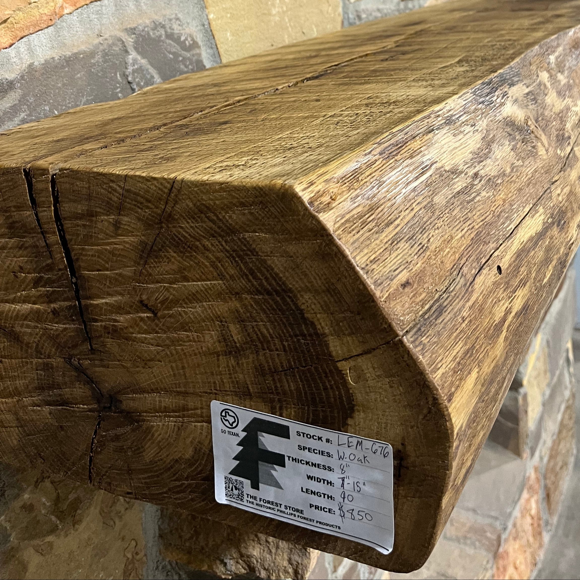 Live edge white oak fireplace mantel with natural grain and rustic finish mounted on a stone wall.
