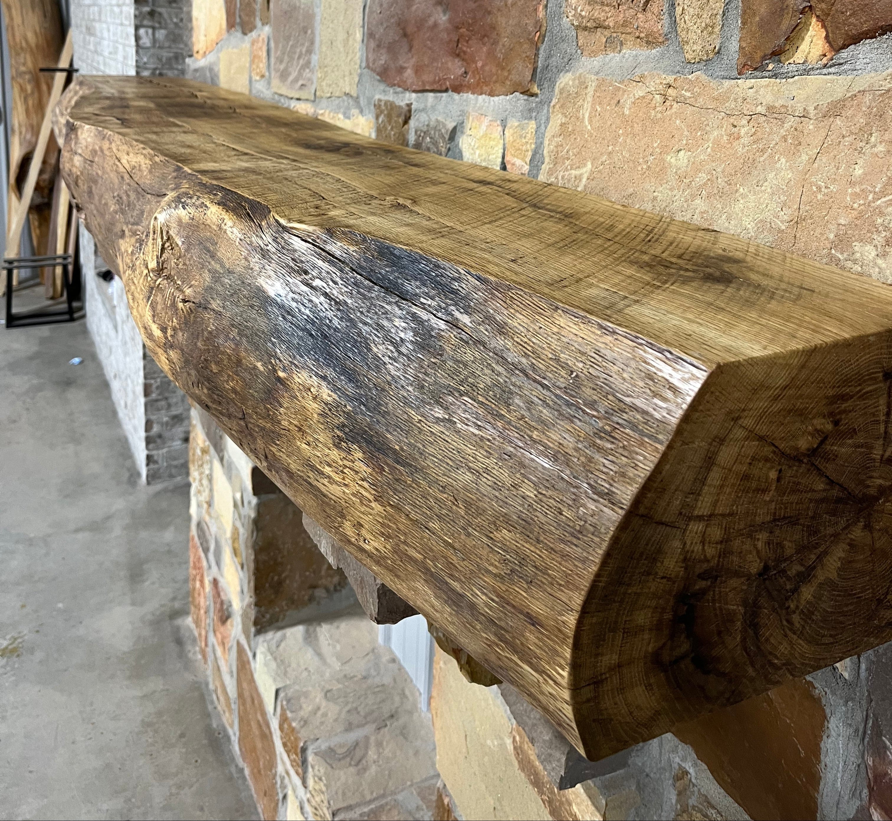 Live edge white oak fireplace mantel with natural grain and rustic finish mounted on a stone wall.