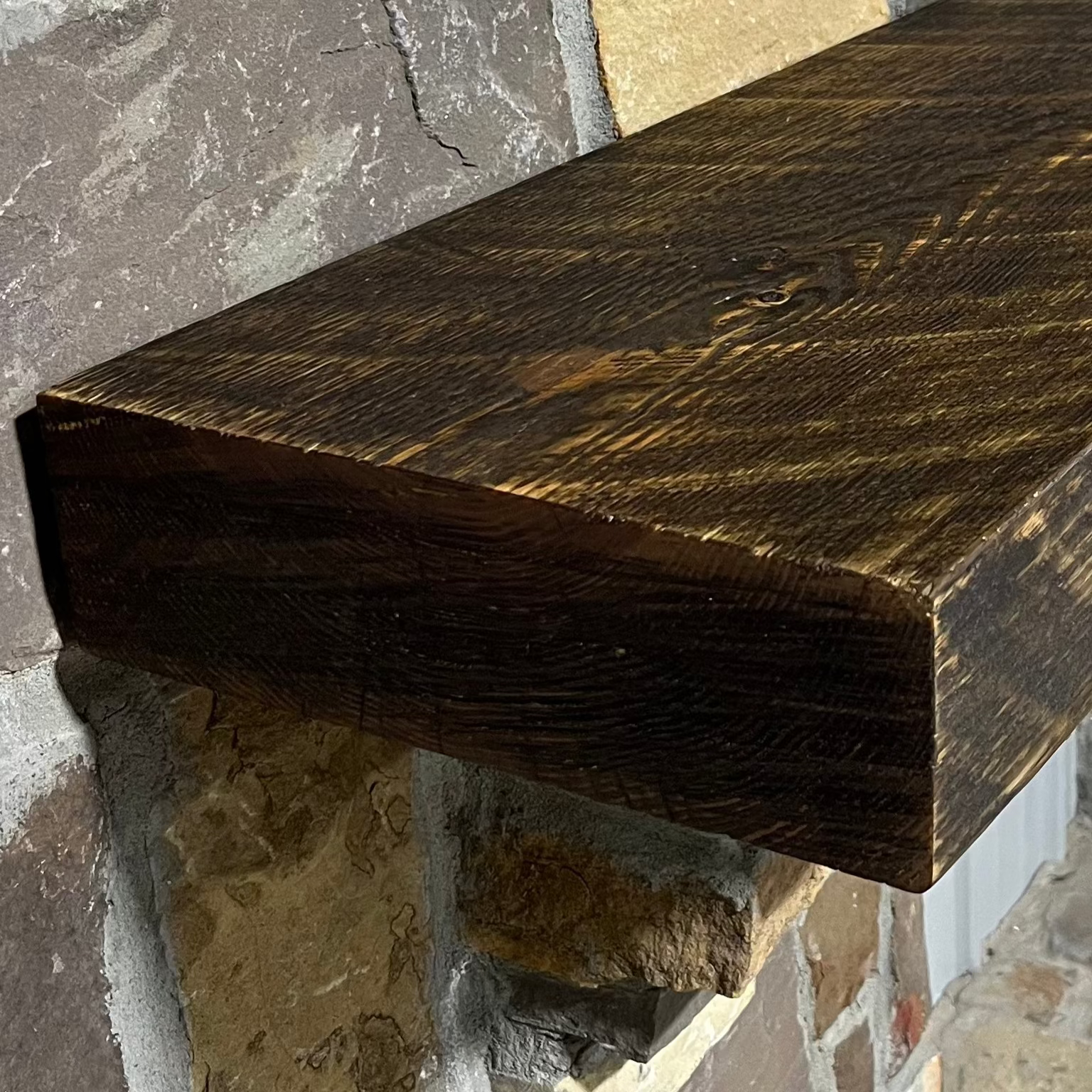Solid pine beam fireplace mantel mounted on a stone wall.