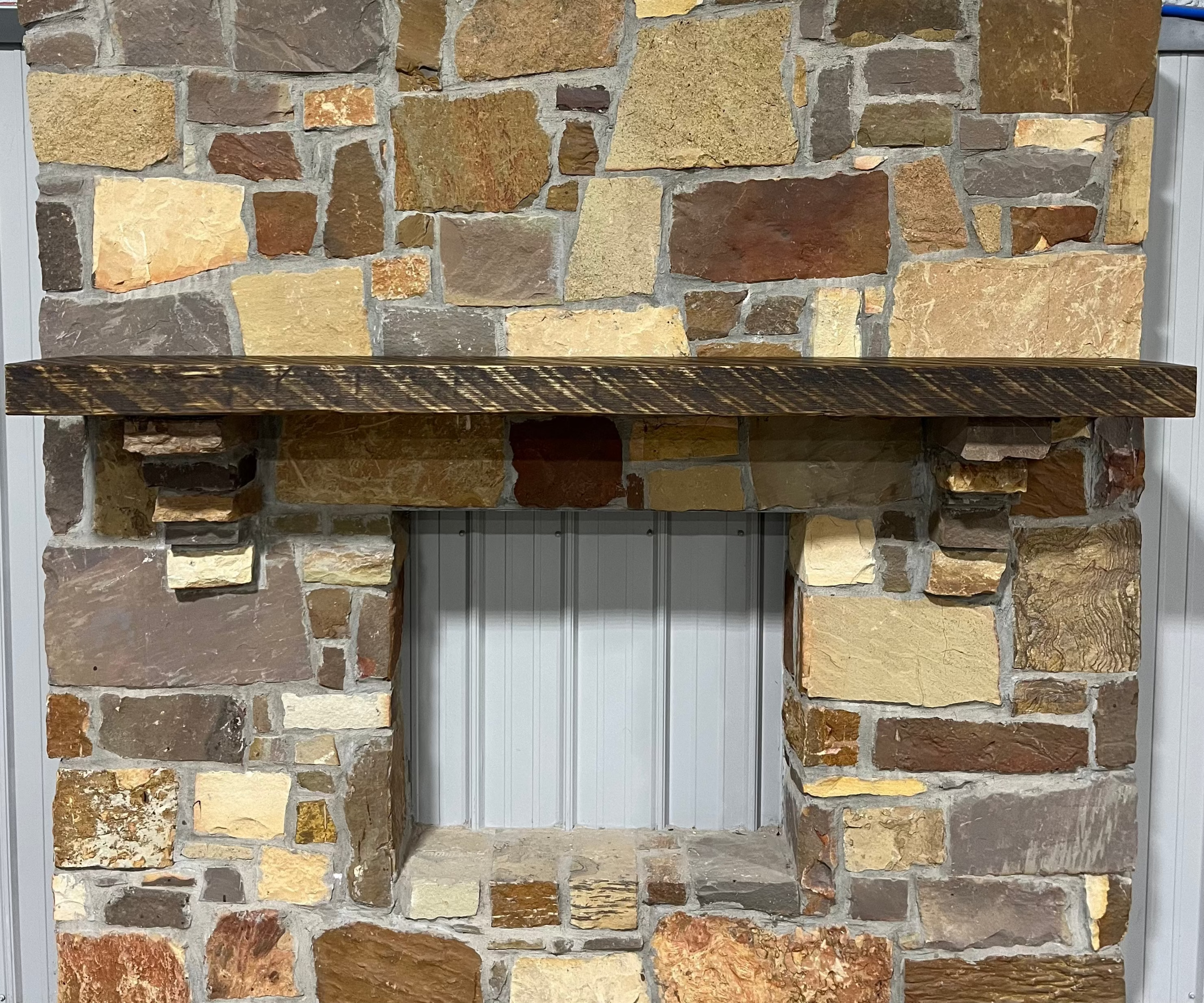 Solid pine beam fireplace mantel mounted on a stone wall.