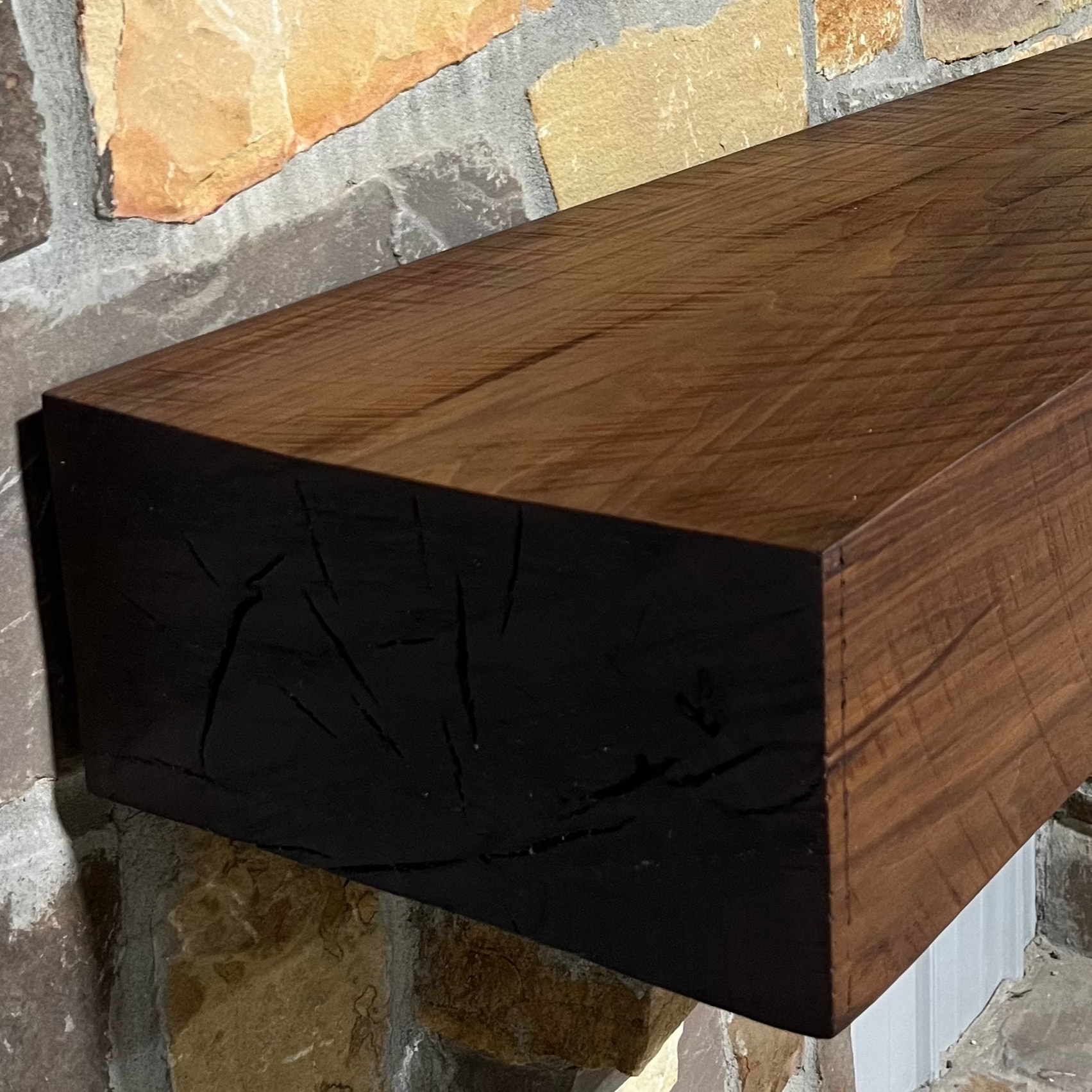 Solid walnut beam fireplace mantel with mounted on a stone fireplace wall.