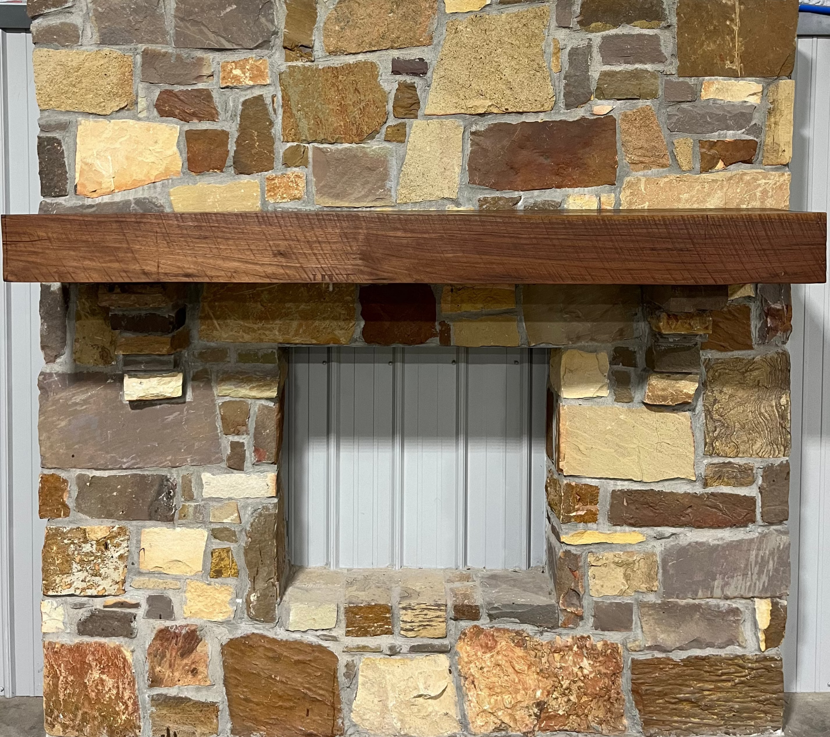 Solid walnut beam fireplace mantel with mounted on a stone fireplace wall.
