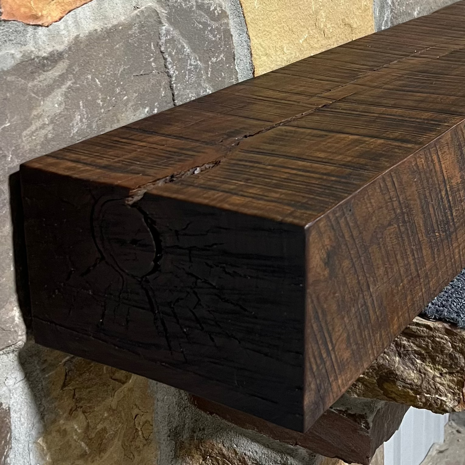 Solid walnut beam fireplace mantel with mounted on a stone fireplace wall.