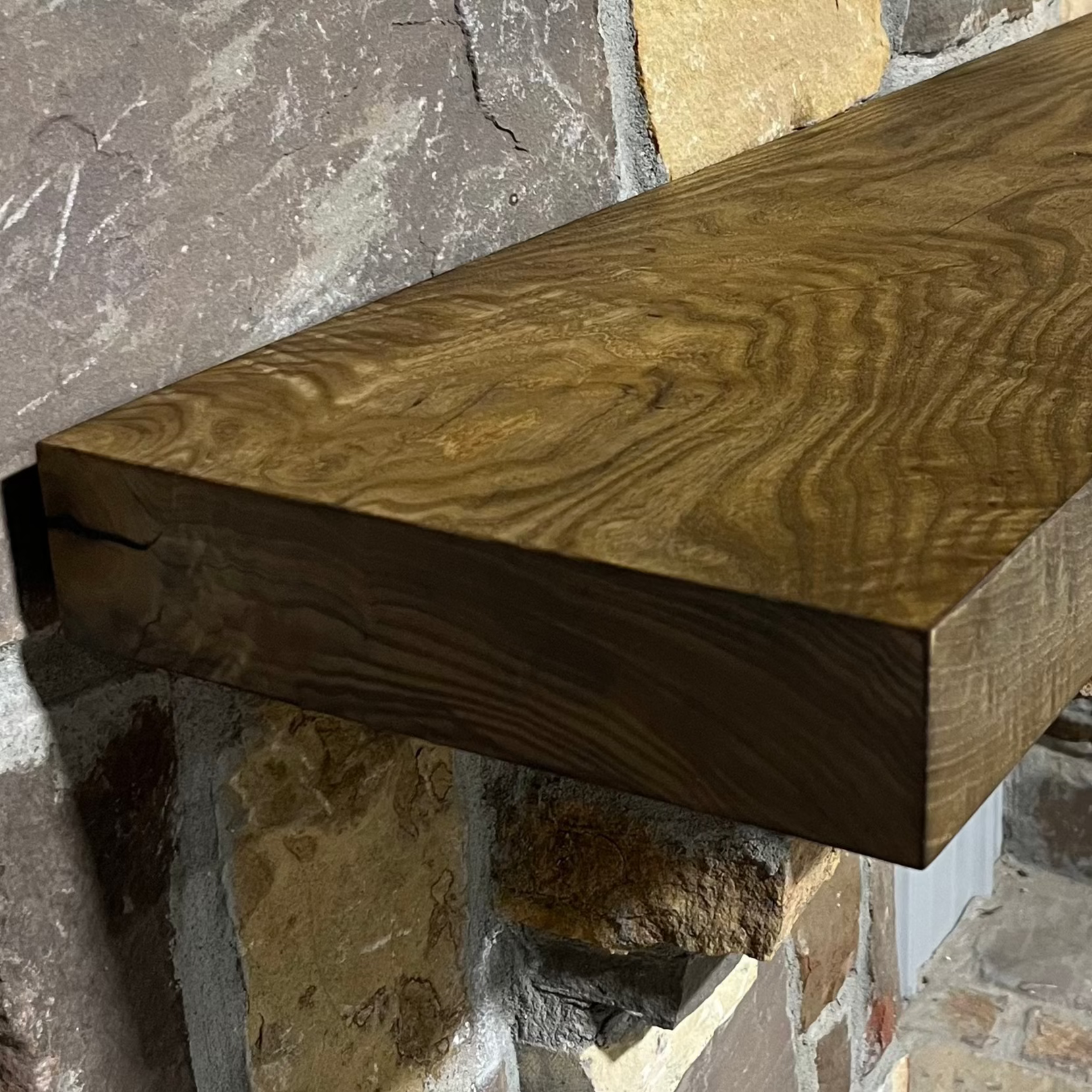 Solid weathered ash fireplace mantel mounted on a stone wall.