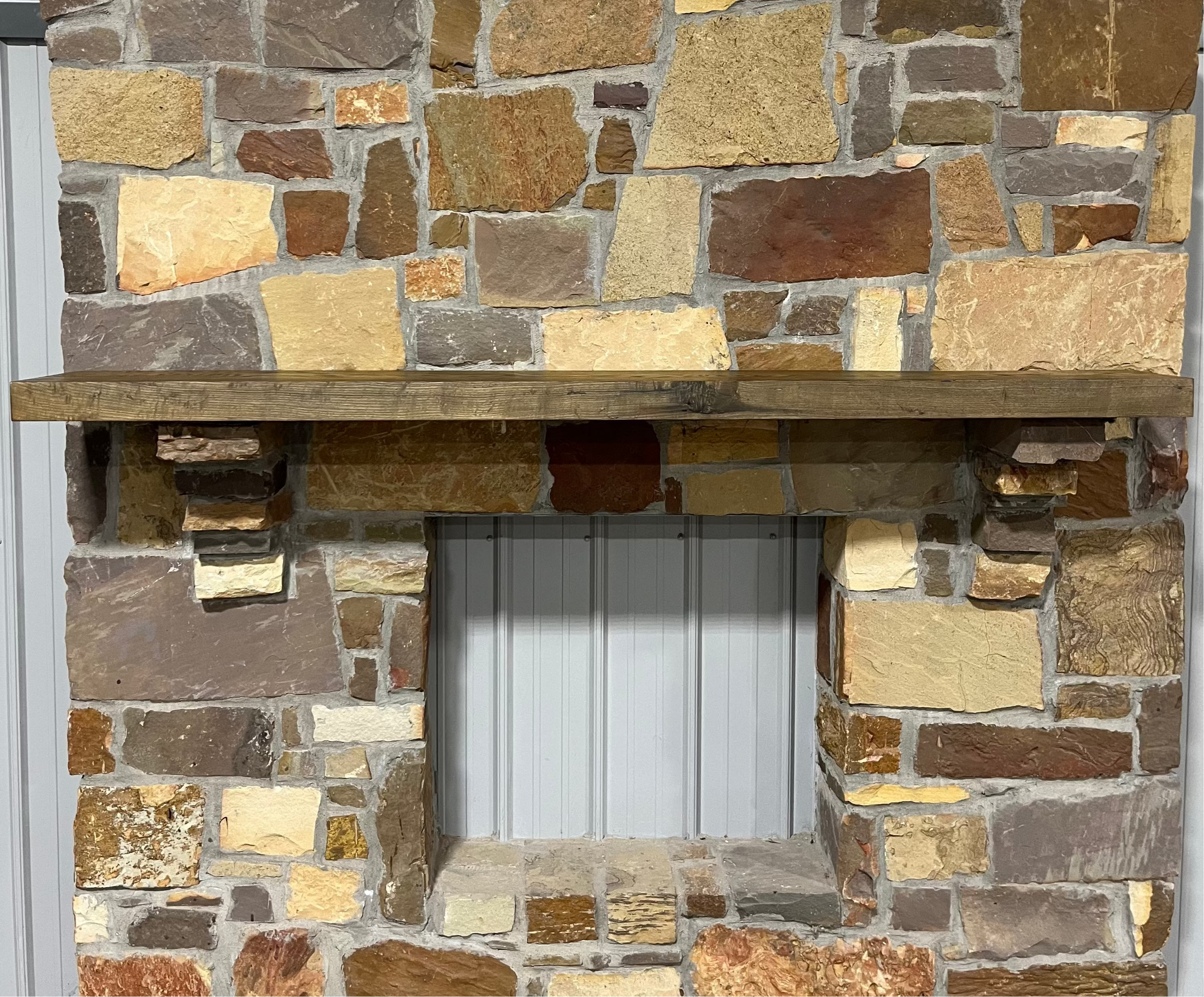 Solid weathered ash fireplace mantel mounted on a stone wall.