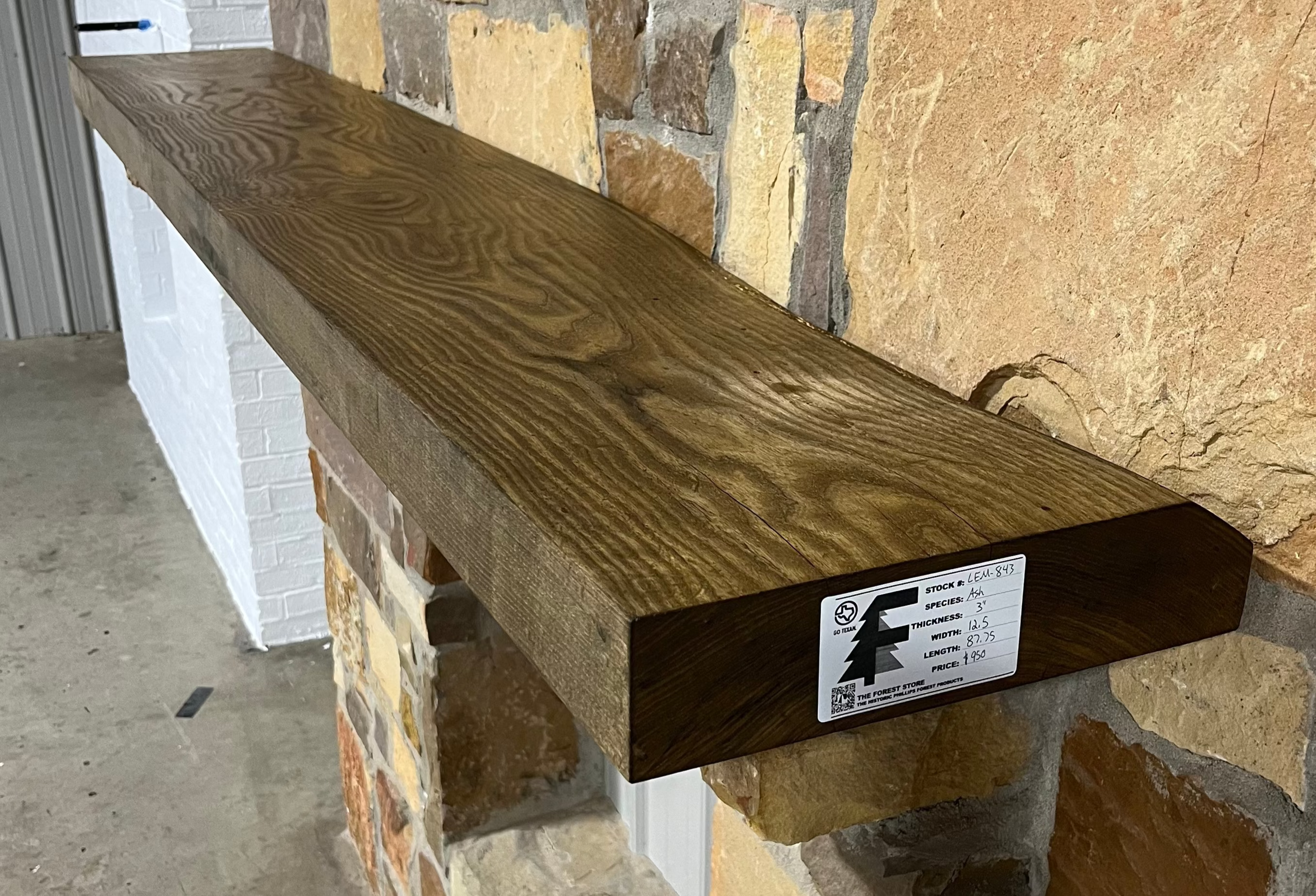 Solid weathered ash fireplace mantel mounted on a stone wall.