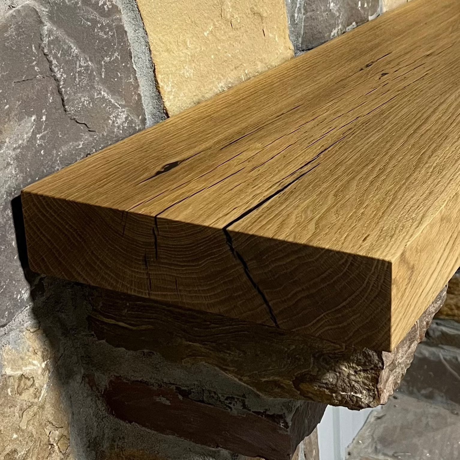 Solid white oak beam fireplace mantel mounted on a stone wall.