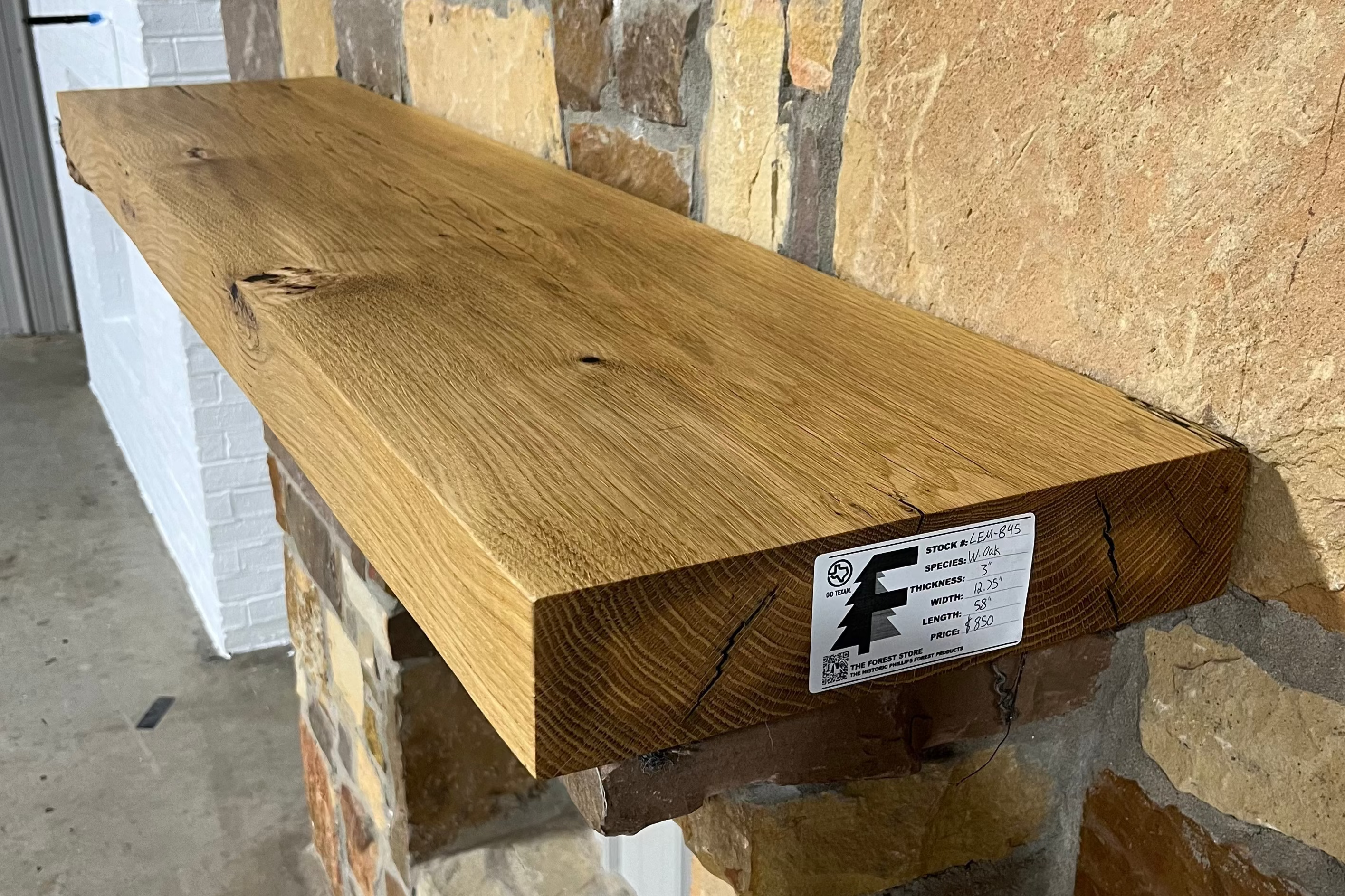 Solid white oak beam fireplace mantel mounted on a stone wall.