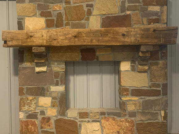 hand hewn reclaimed beam fireplace mantel mounted to stone wall
