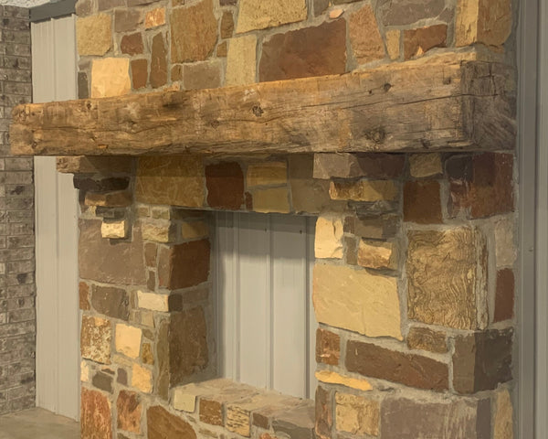 hand hewn reclaimed beam fireplace mantel mounted to stone wall
