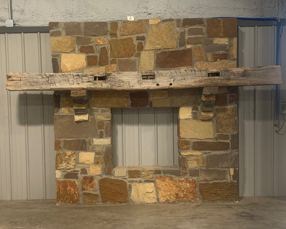 hand hewn reclaimed beam fireplace mantel mounted to stone wall
